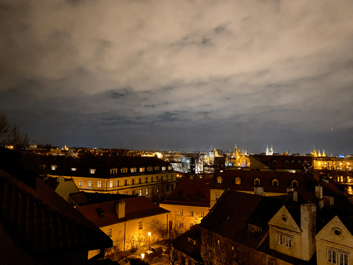Night view across the rooftops of Malá Strana towards the lit spires of Prague